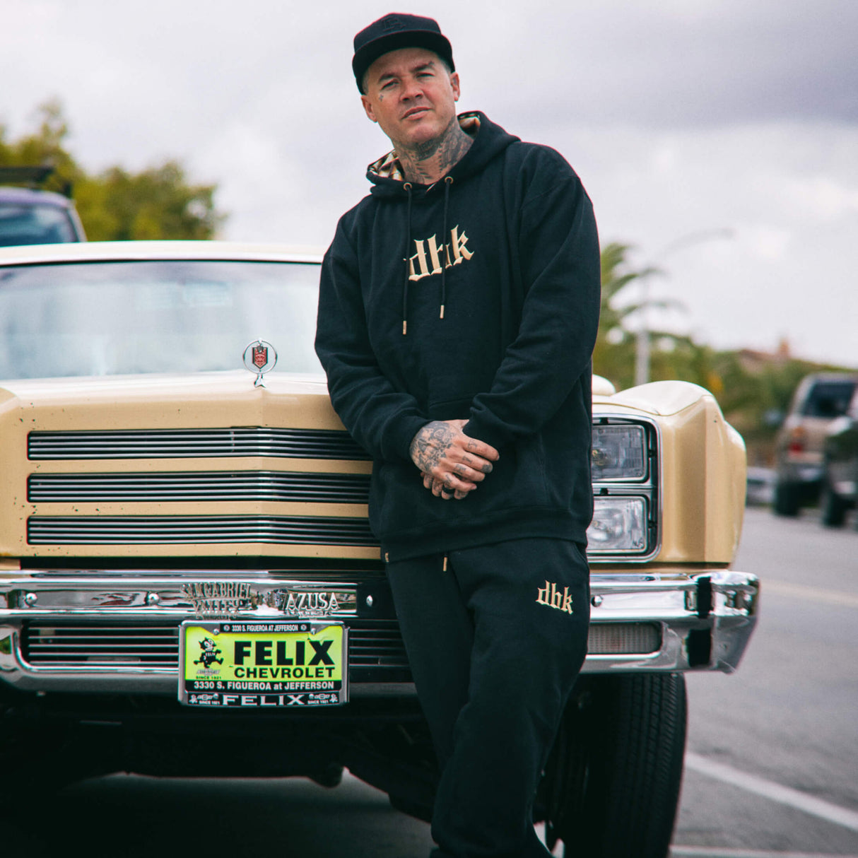 Black hoodie with gold chest logo and drawstring hood, worn with matching joggers.