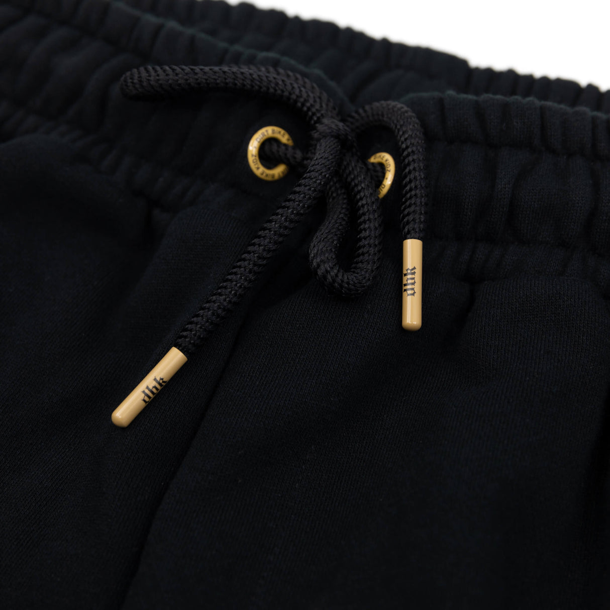 Black sweatpants waistband with braided drawstrings and gold-tipped aglets detail.