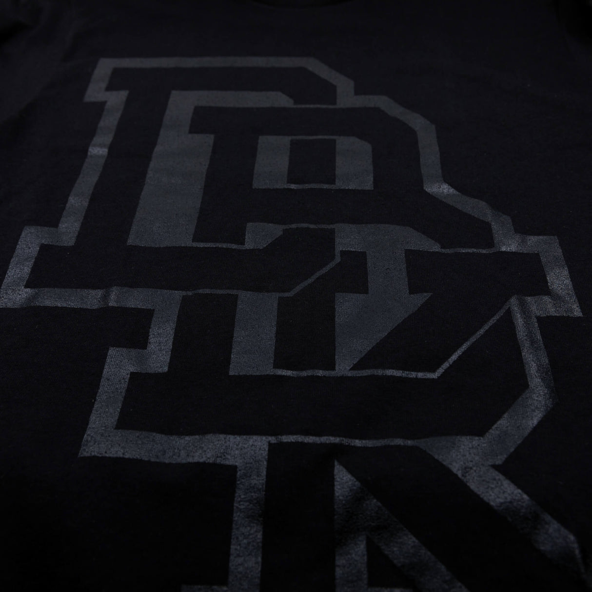 Youth premium tee, close-up of front logo graphic in dark gray on black fabric