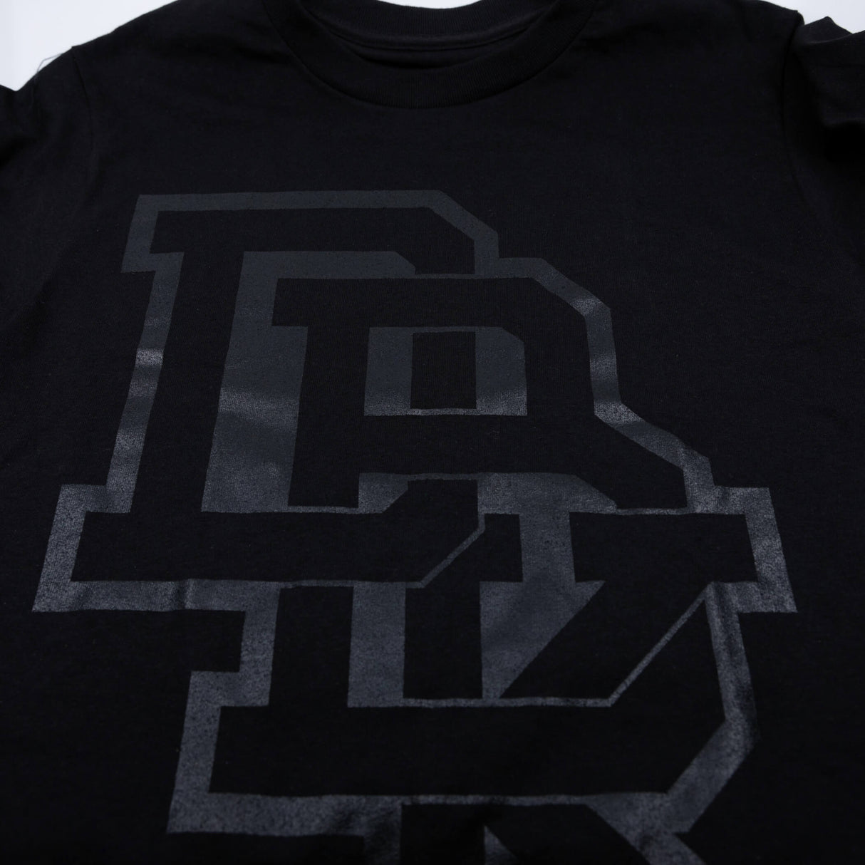 Youth premium tee, close-up of black front graphic logo in dark gray
