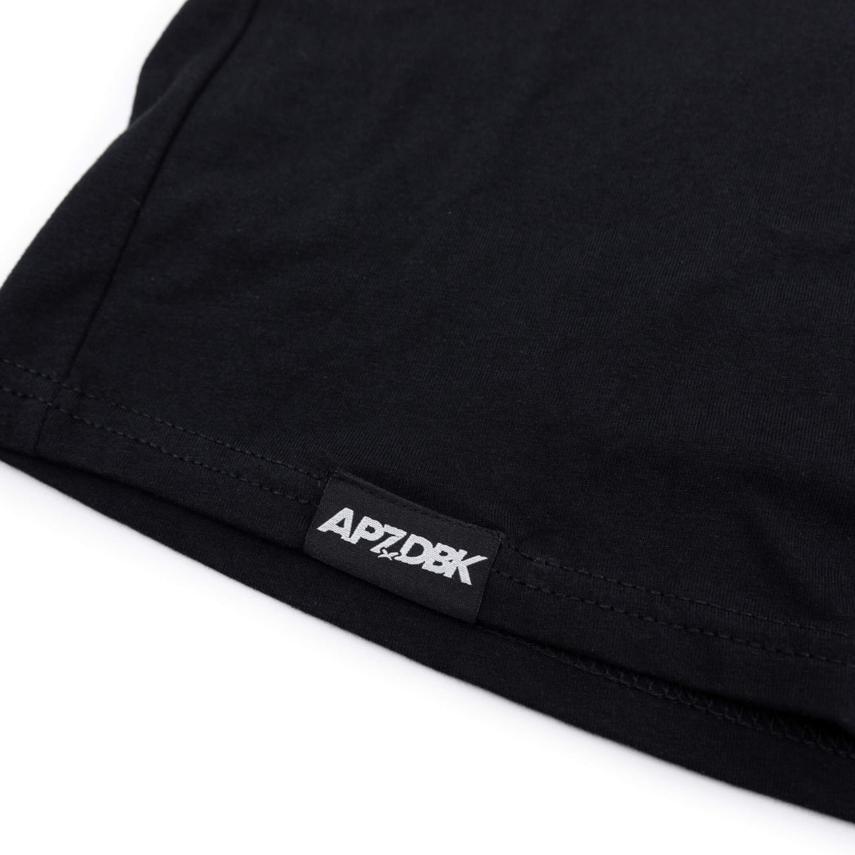 Youth black T-shirt hem with small AP7-DBK label tag on sleeve edge.