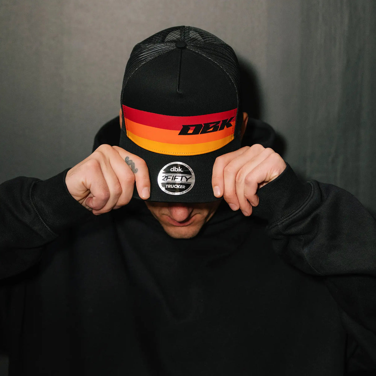 Black trucker cap with orange-red-yellow stripe and DBK logo, head-on view