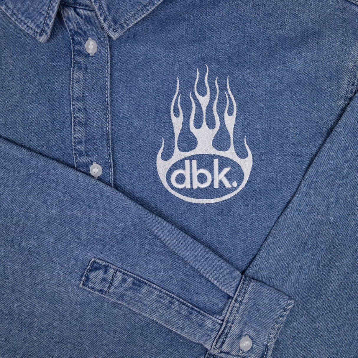 Blue denim shirt logo detail with button placket and cuff at sleeve opening.
