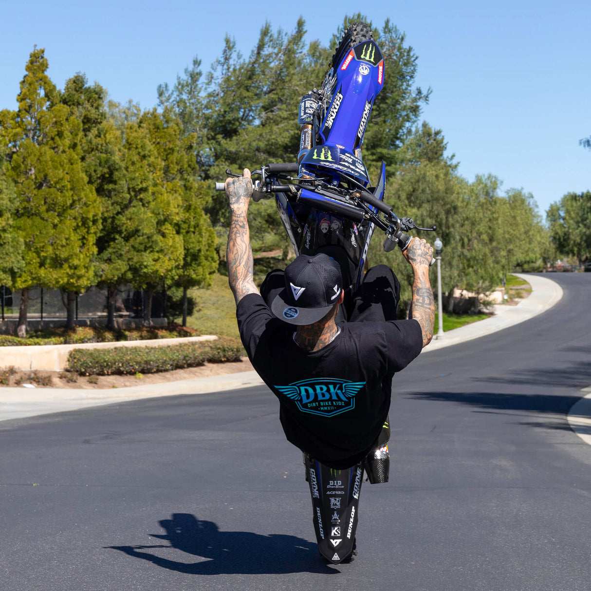 Black T-shirt on a rider’s back with blue DBK logo graphic.