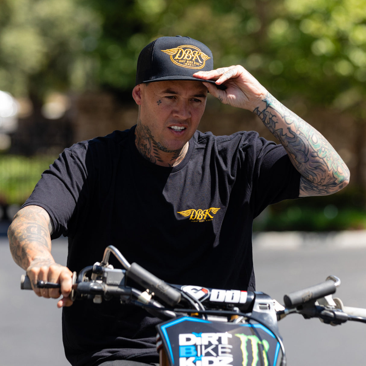 Black trucker cap with yellow DBKR wing logo on front, worn by rider