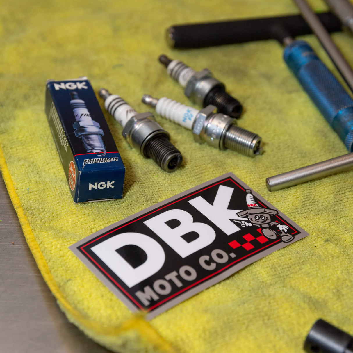 DBK Moto Co sticker with large DBK lettering and cartoon character, on yellow cloth