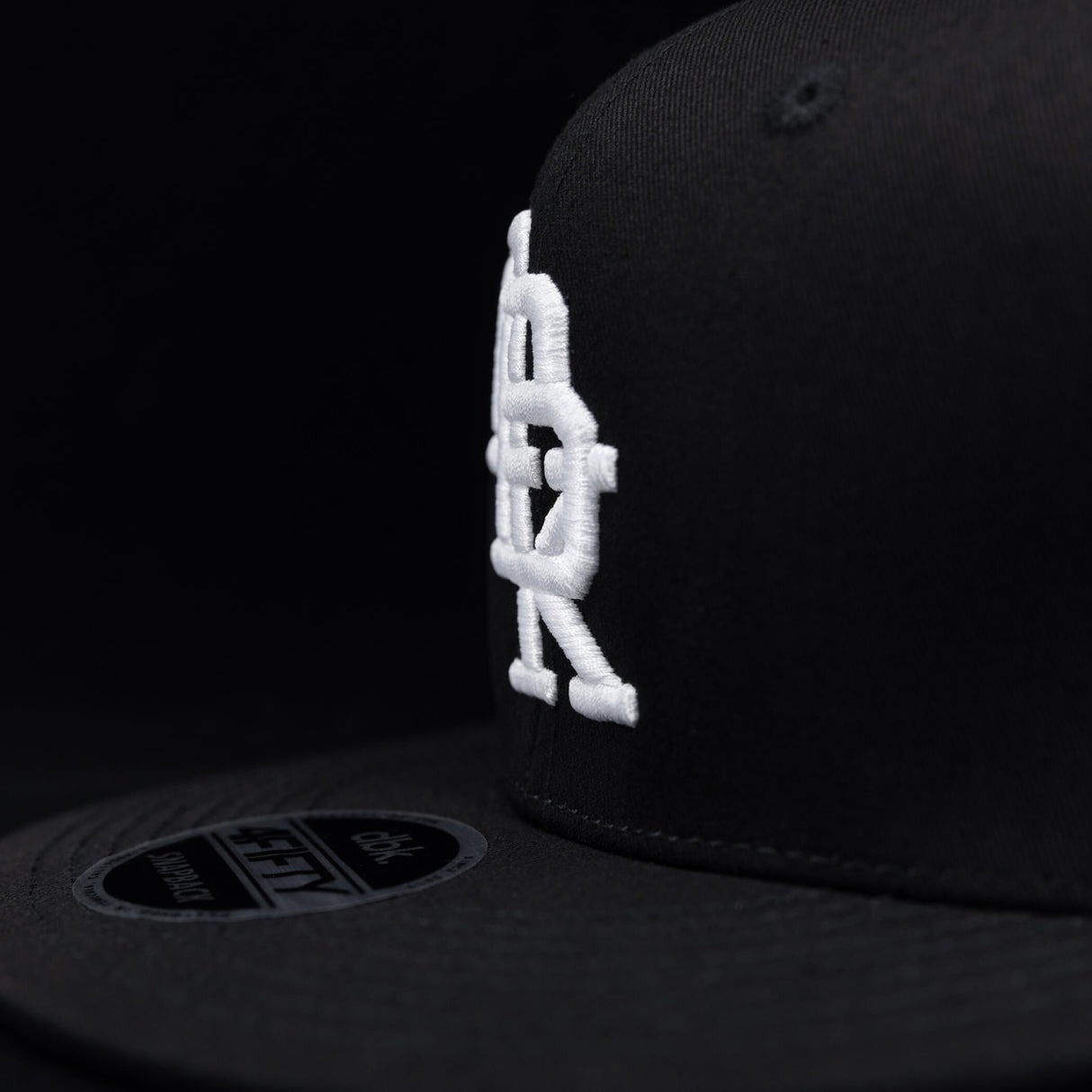 Black snapback cap side profile with white DBK embroidery near the brim