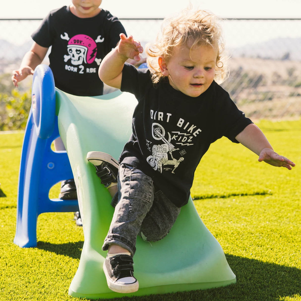 Black toddler T-shirt with front bike rider graphic, child on outdoor playground
