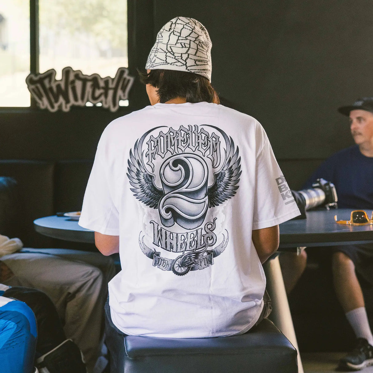 White crew-neck T-shirt with large back print of winged motorcycle emblem.