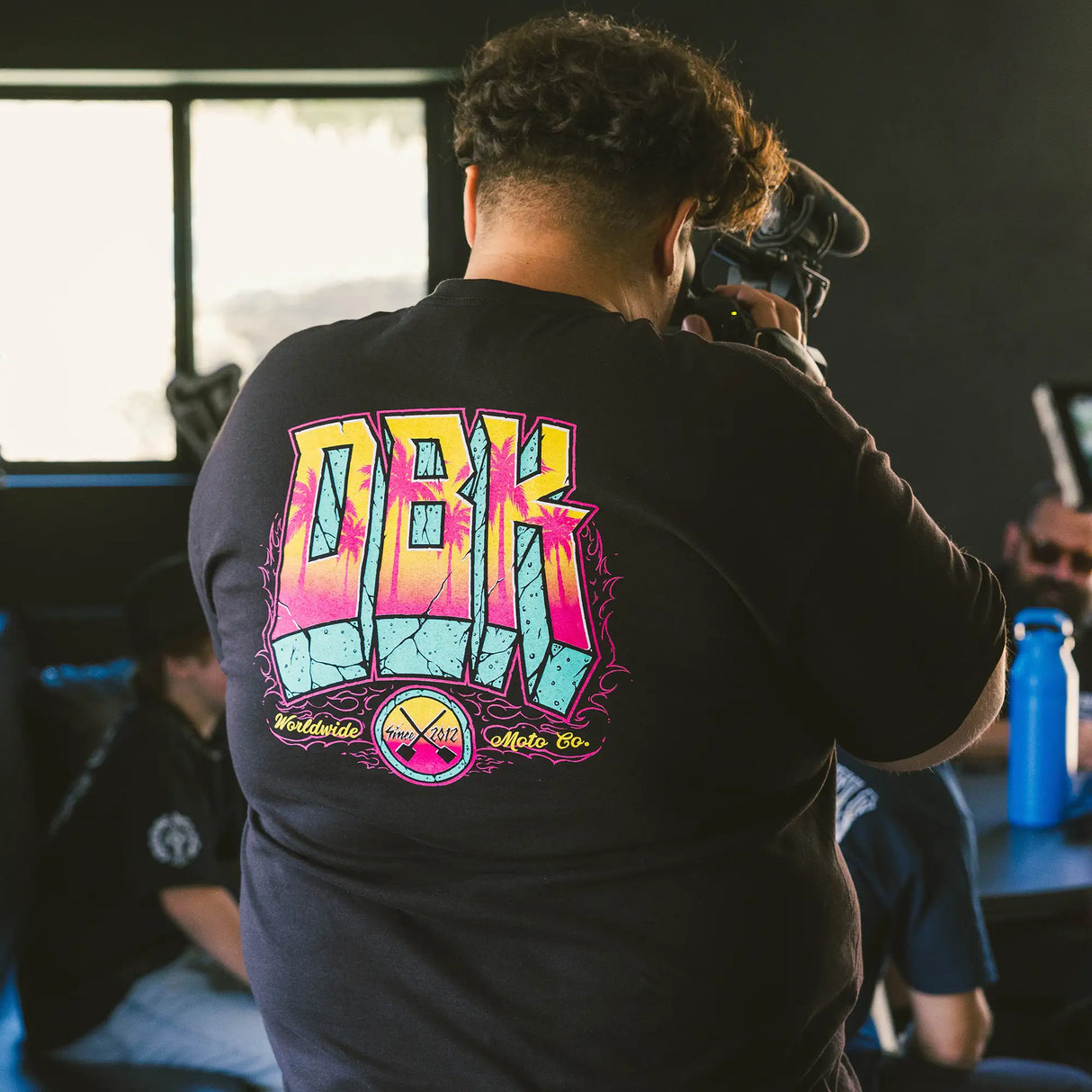 Black crewneck tee with multicolor DBK back graphic worn by person, close view