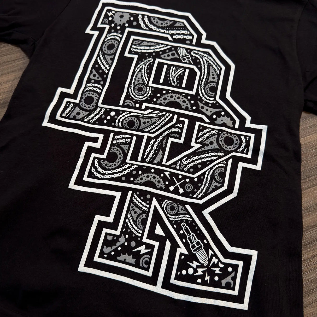 Close-up of black youth tee with white patterned letter graphic and small icon details