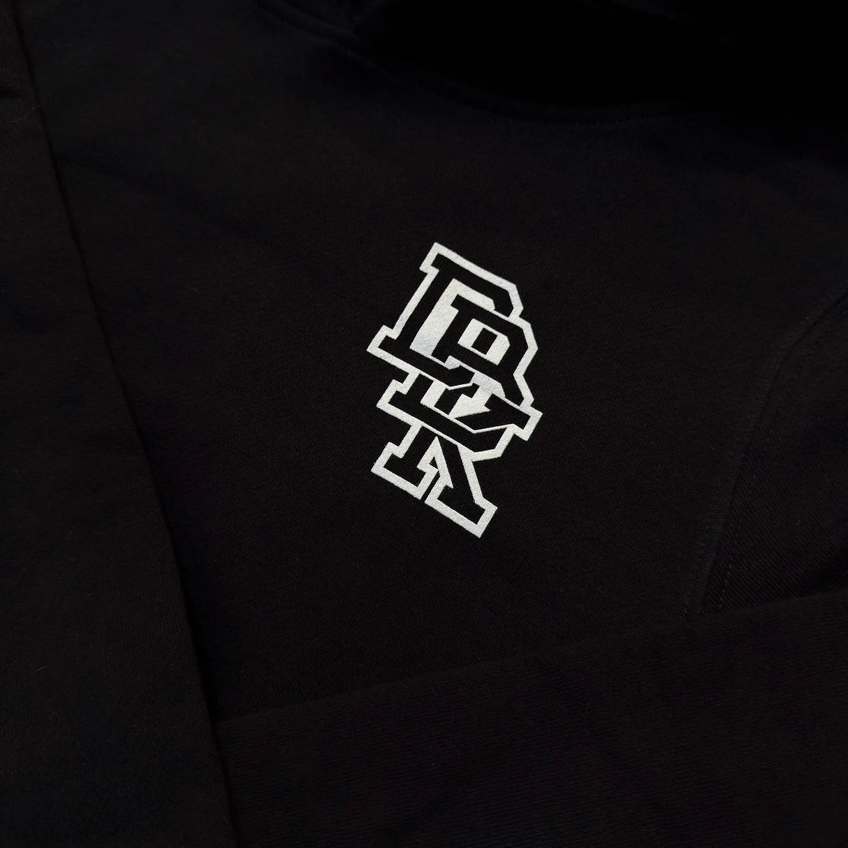 Close-up of black hoodie fabric with small white logo on the left sleeve hem