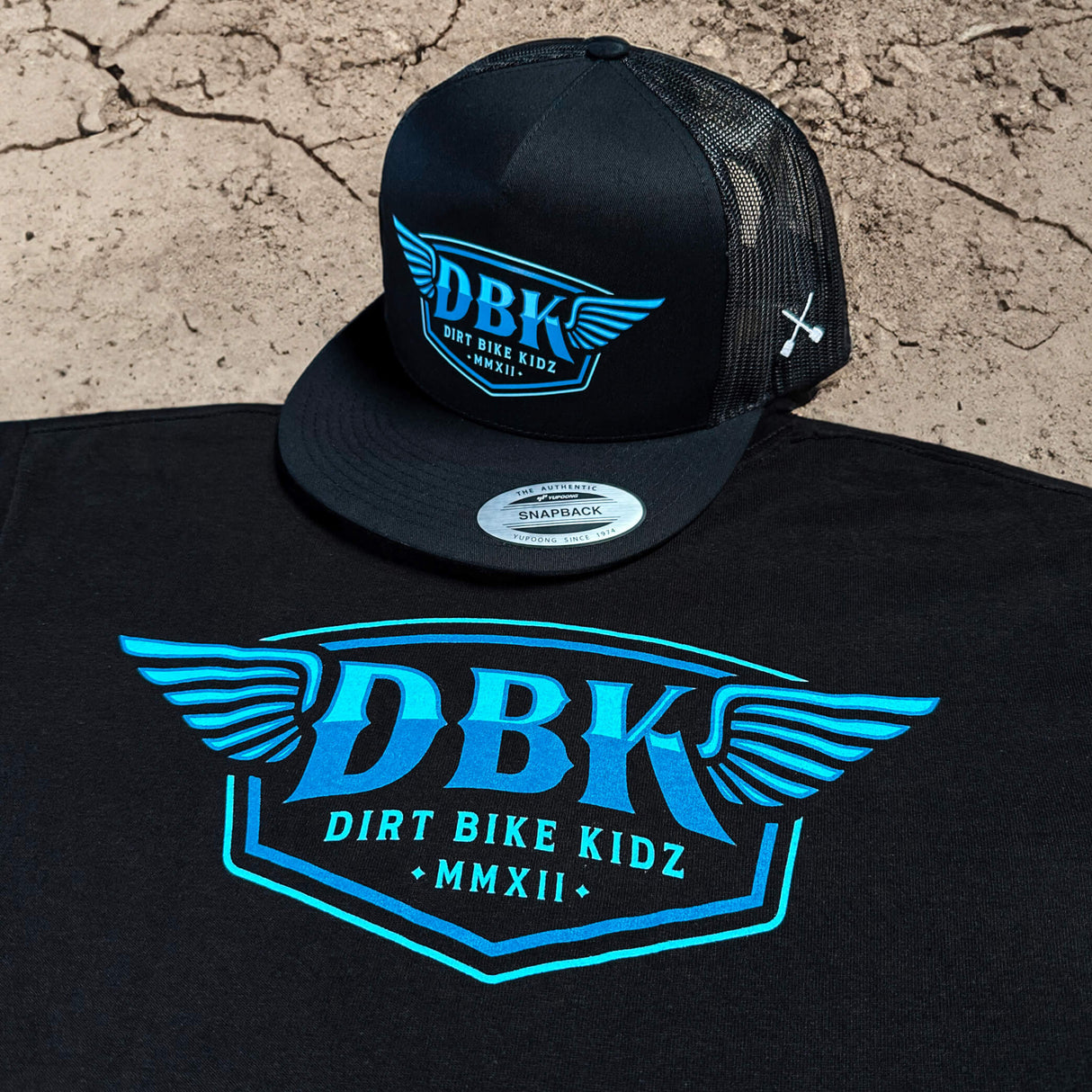 Black T-shirt with large blue DBK graphic print and small logo text below.