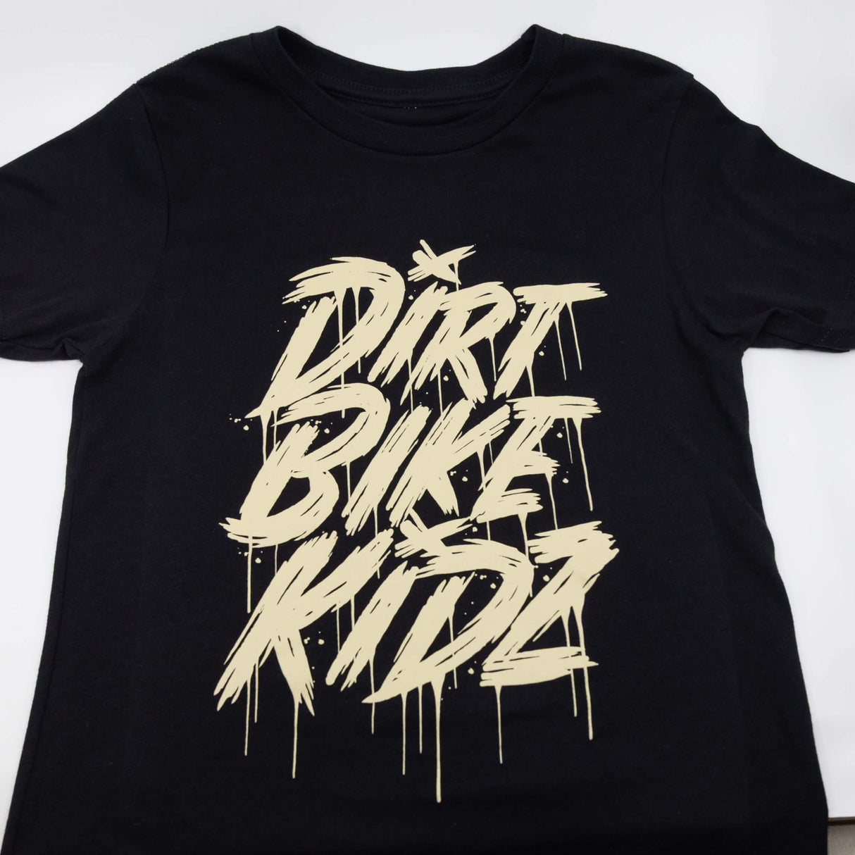 Black youth tee close-up with centered beige DRRT BIKE RIDE graphic print.