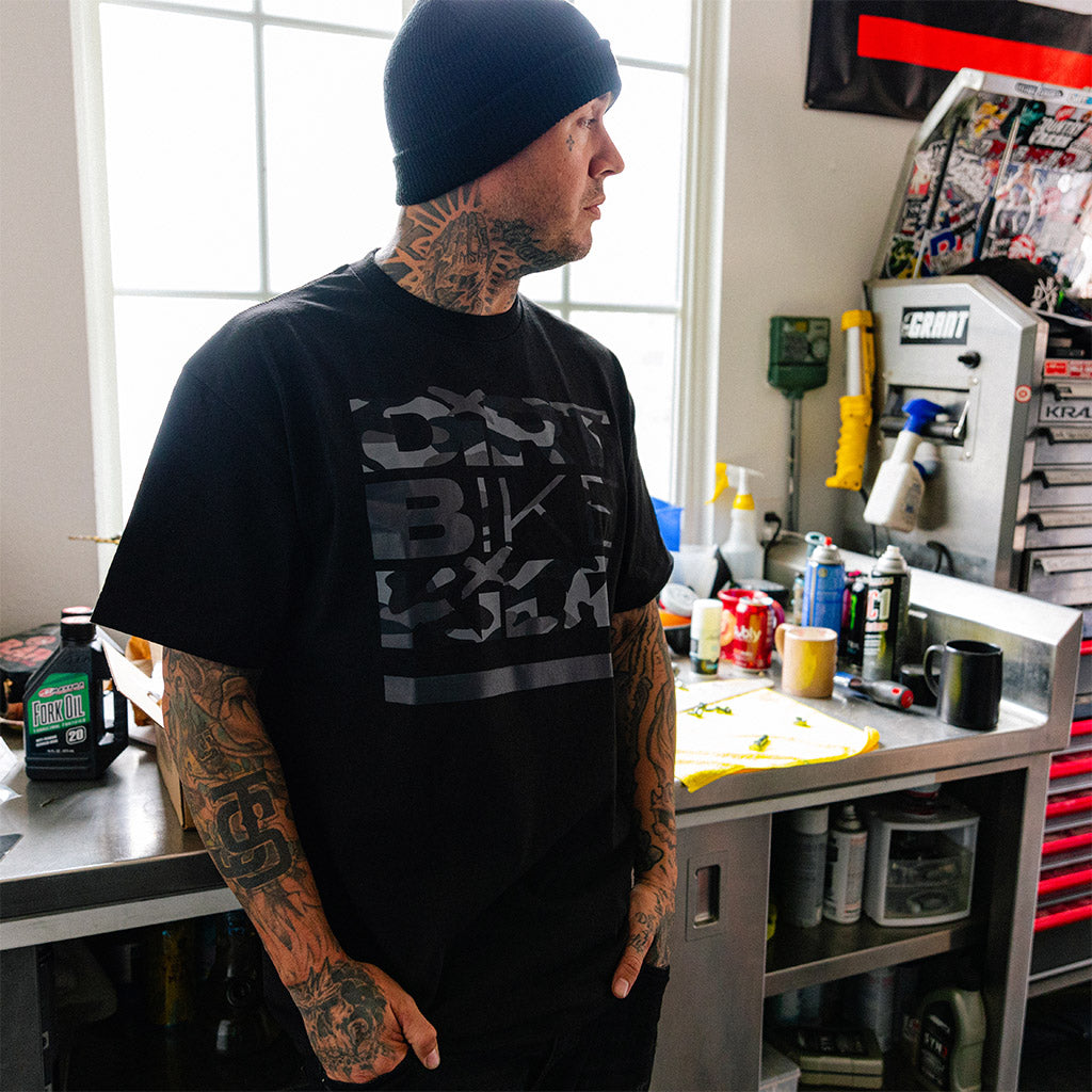 Black T-shirt worn by man, side view; large camo-style front graphic.