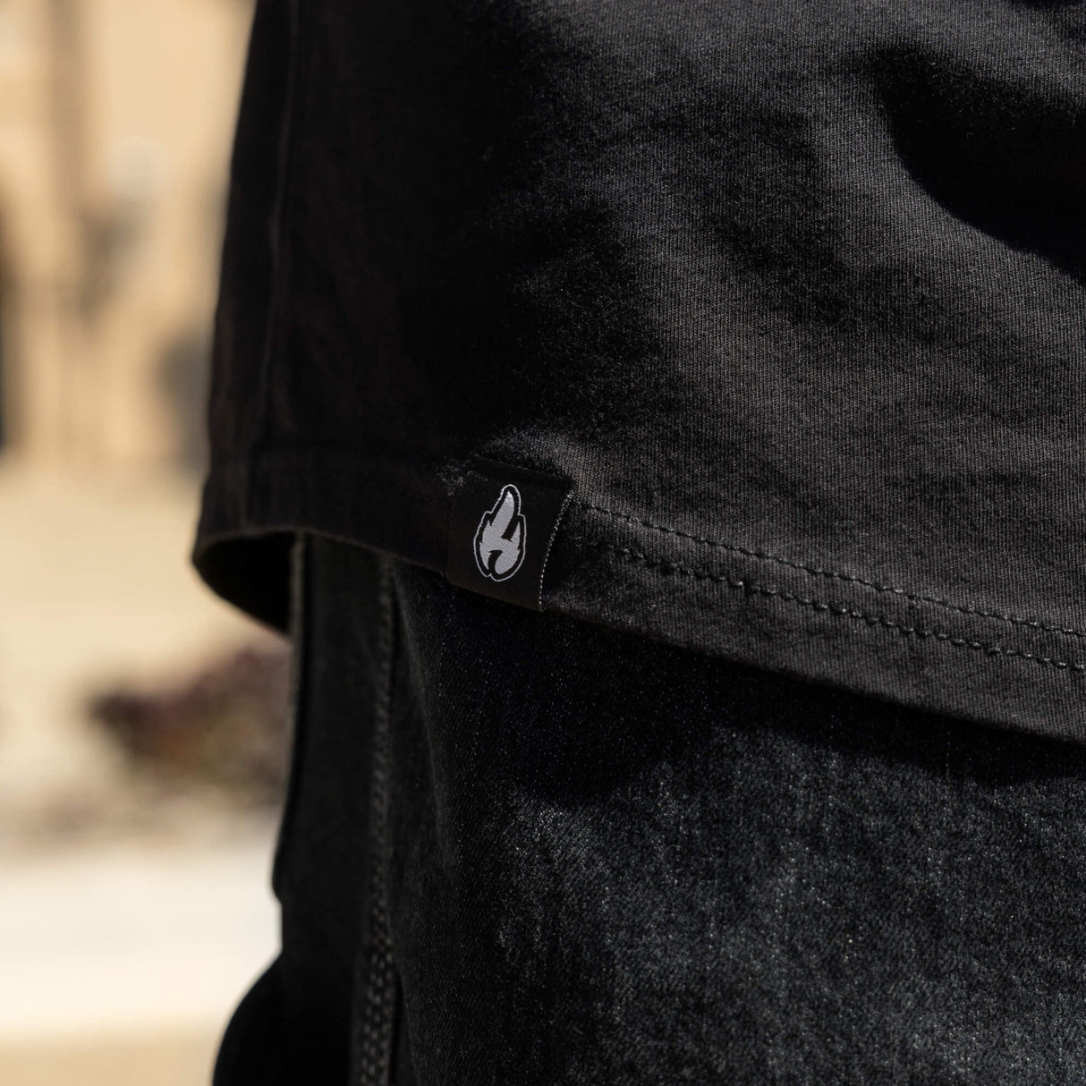 Black varsity tee close-up of side seam and small white logo patch
