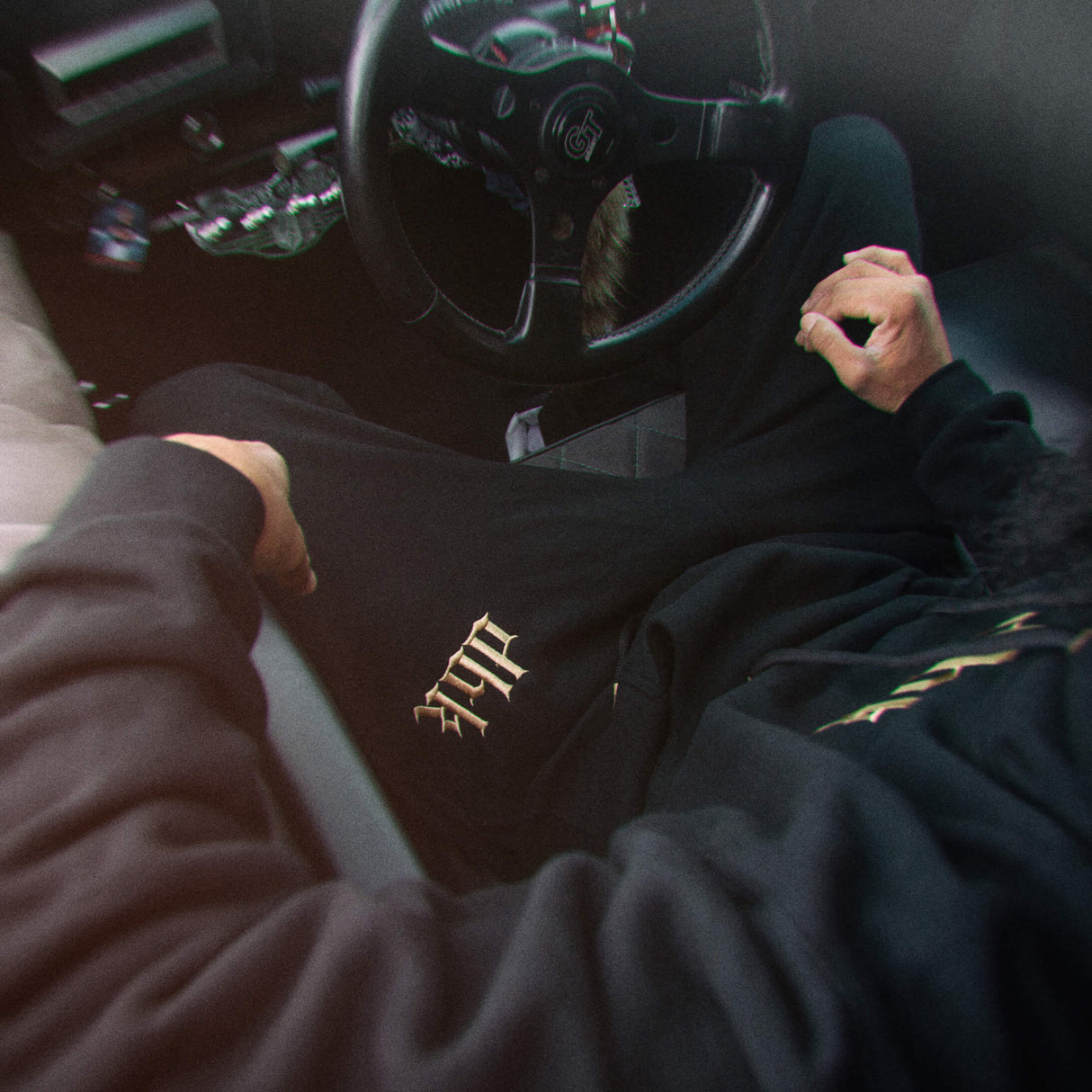Black sweatpants with gold patterned logo patch on the leg hem area.
