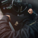 Black sweatpants with gold patterned logo patch on the leg hem area.