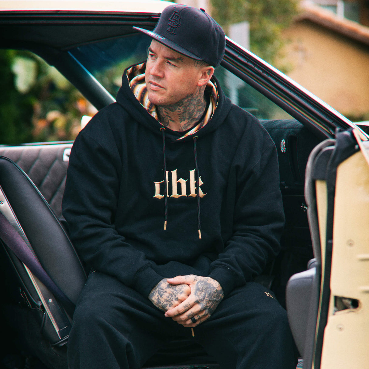 Black hoodie with gold chest logo and striped inner hood lining, worn outdoors.