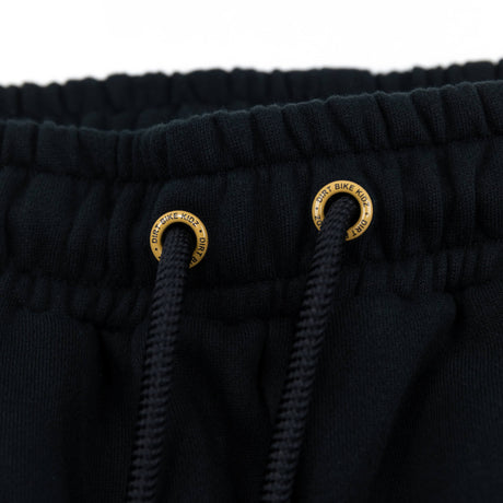 Black sweatpants drawstring eyelets with gold emblem rings at the waistband.