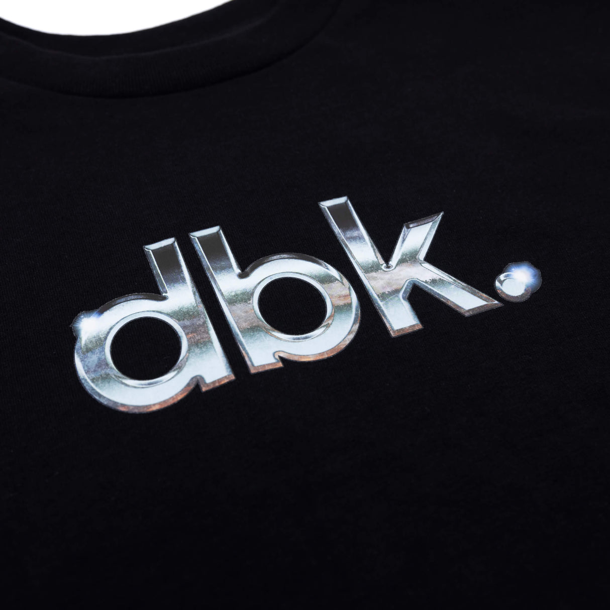Black T-shirt close-up of metallic silver dbk logo print on chest.