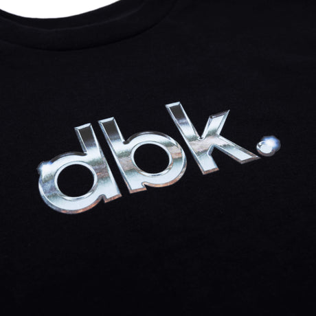 Black T-shirt close-up of metallic silver dbk logo print on chest.