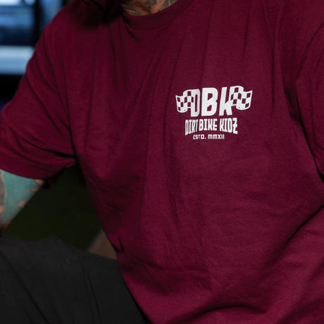 Burgundy graphic T-shirt on a seated model, showing the DBK chest logo print
