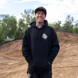 Black pullover hoodie with hood drawstrings and small gold logo on chest
