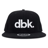 Black snapback cap front view with large white dbk logo and flat brim.