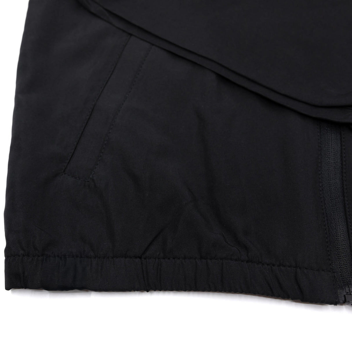 Black youth windbreaker hem close-up with elastic cuffs and visible side zipper tab