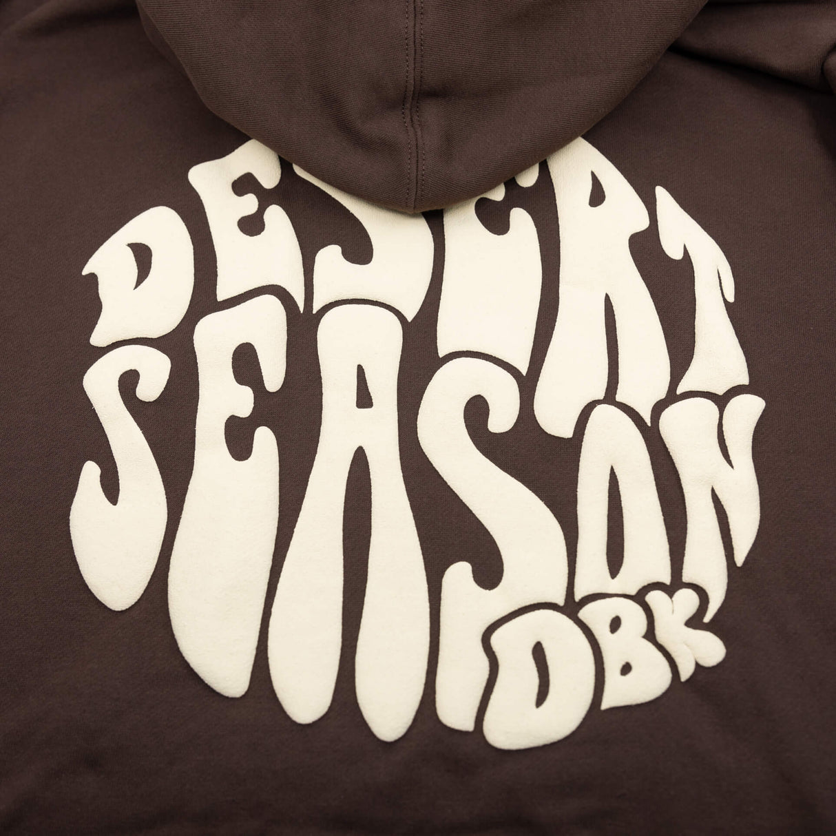 Close-up: oversized white Desert Season graphic on the back of a dark brown hoodie