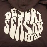 Close-up: oversized white Desert Season graphic on the back of a dark brown hoodie
