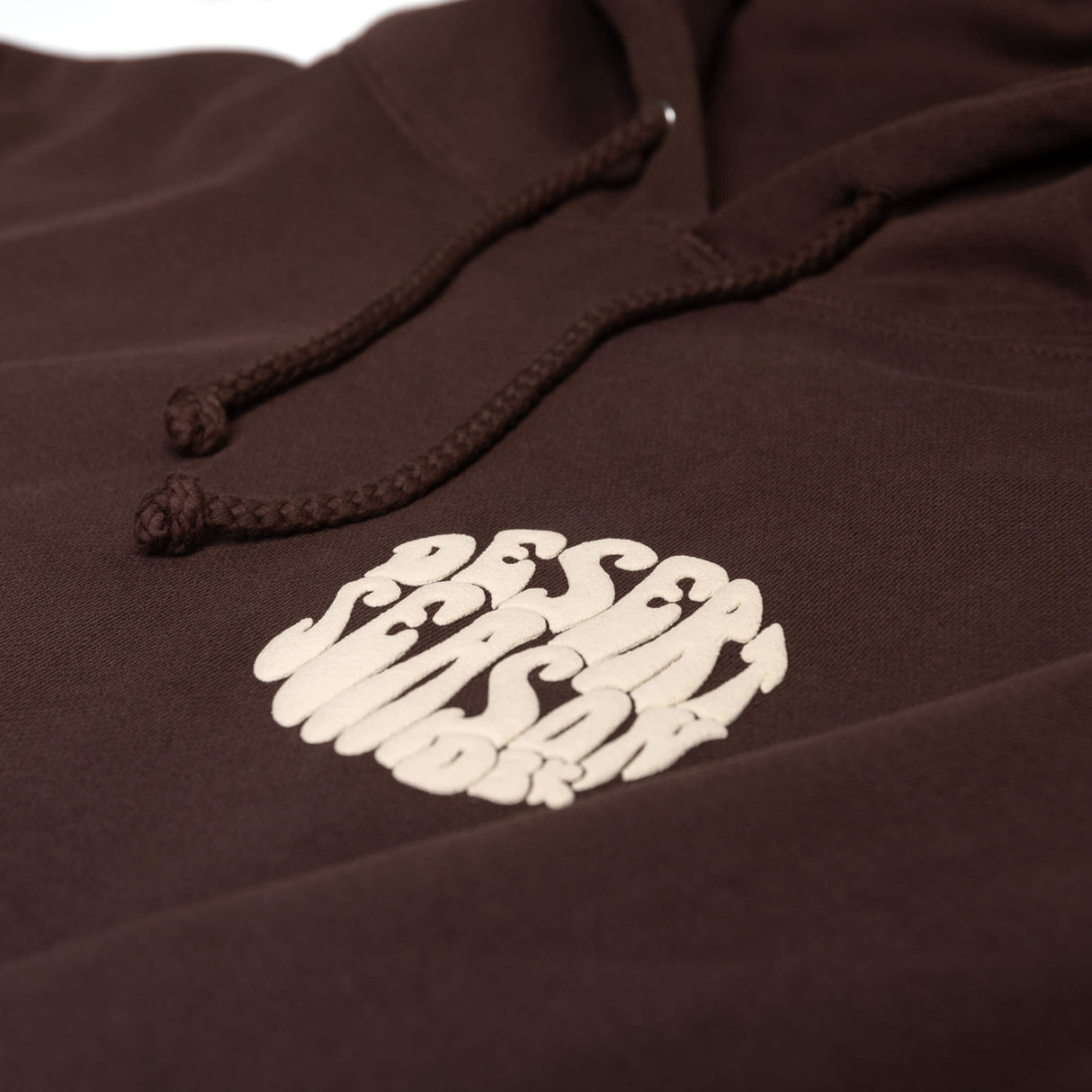 Close-up of dark brown hoodie drawstrings and small white logo on the front