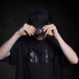 Black dbk graphic T-shirt on model, holding cap with both hands