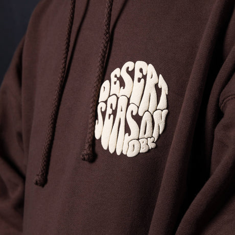 Dark brown hoodie logo patch on front with drawstrings and kangaroo pocket seam