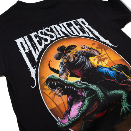 Black youth T-shirt large front graphic showing a cowboy punching while riding a green crocodile.