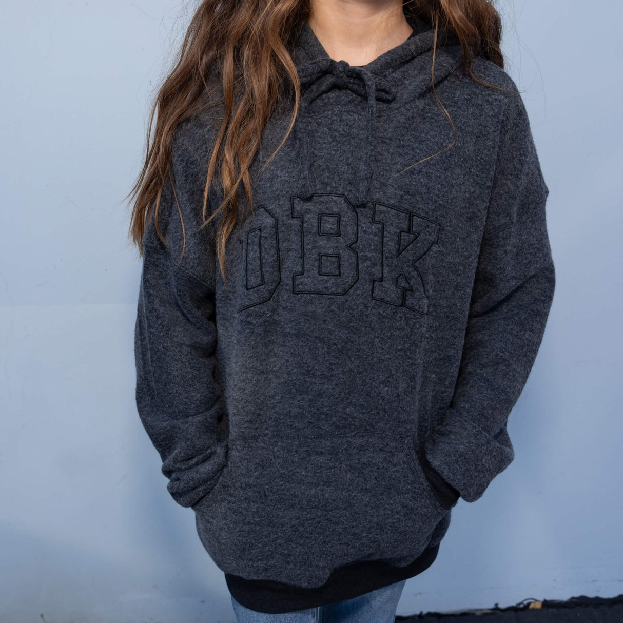 Women’s dark charcoal pullover hoodie worn with drawstring hood and front logo