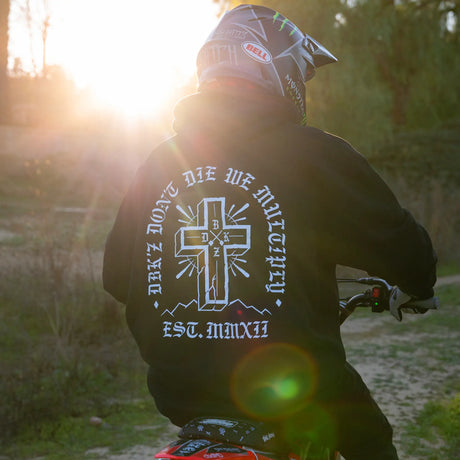 Black zip hoodie with large white cross back graphic, worn outdoors.