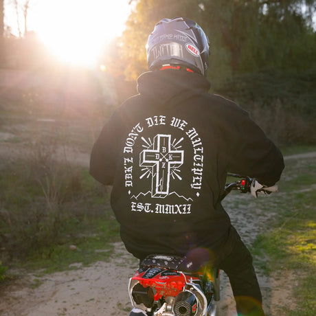Black zip hoodie with white cross back graphic, worn outdoors with cap.