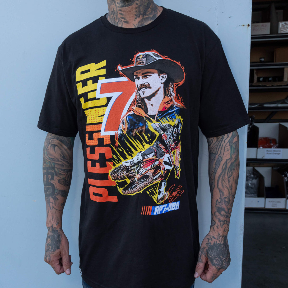 Black AP7 graphic T-shirt with racing-figure illustration and AP7×DBK logo on chest.
