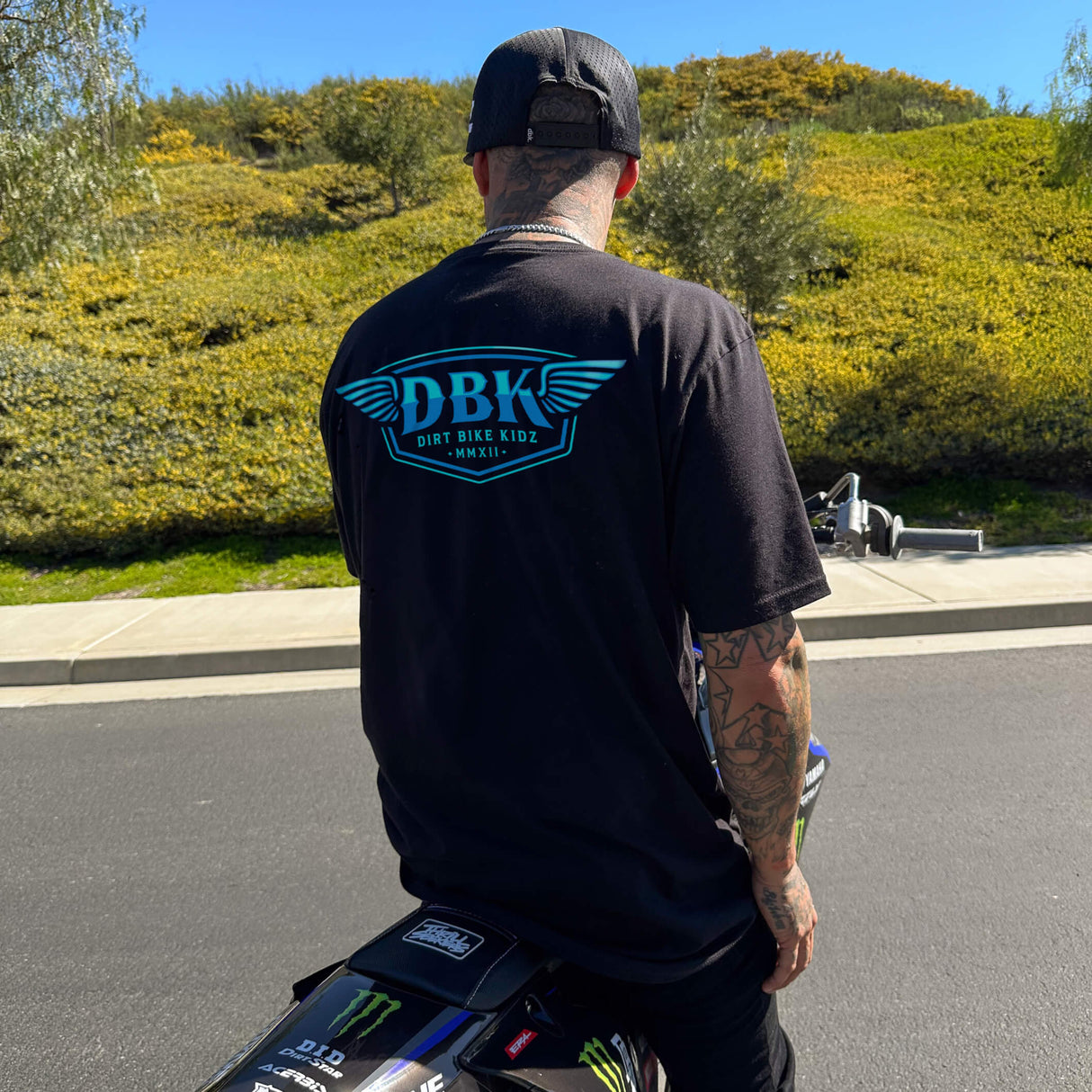 Black T-shirt, back view, with blue DBK logo graphic centered.