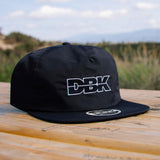 Black snapback cap with DBK logo on the side panel for wear.