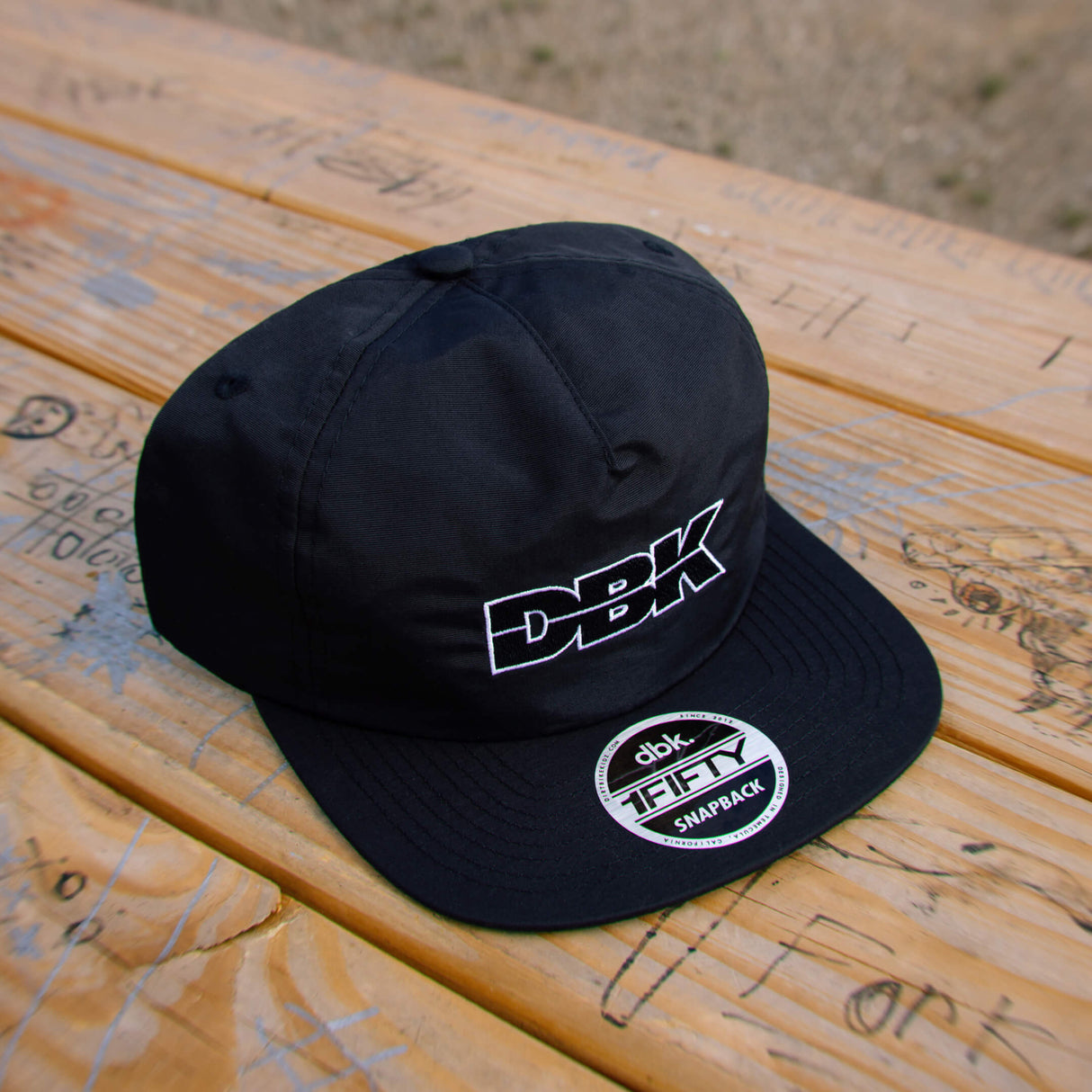 Black snapback cap with DBK logo and 1FIFTY snapback patch on brim.