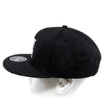 Black snapback cap from back angle with visible eyelets on crown.