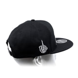 Black snapback cap with curved brim and white hand emblem on side panel