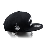 Black snapback cap with curved brim, white hand emblem, and large side lettering