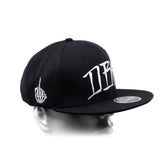 Black snapback cap with curved brim and white side lettering panel detail