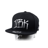 Black baseball cap with white graffiti-style 'DBK' graphic on the front panel