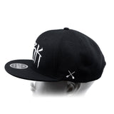 Black baseball cap with white 'DBK' lettering on the side and white crossbones graphic