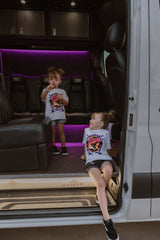 Youth girls white graphic T-shirt worn by a child inside a vehicle, front print visible